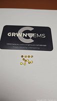 Photo showing 12 small round yellow tourmaline gemstones next to a GRWN Gems business card for scale and branding.