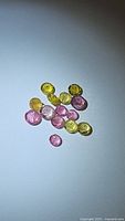 Photo showing natural calibrated pink and yellow round tourmaline gemstones scattered on white surface under direct lighting.