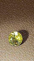 Close-up photo of a round cut yellow-green African sphene gemstone on a textured brown surface showing facets and inclusions.