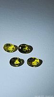 Four oval cut natural sapphires on a white background in daylight showing yellow and blue hues