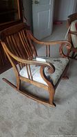 Side view of antique wooden rocking chair showing curved armrest and floral cushioned seat