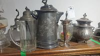 Overview of the lot showing four vintage pieces including a glass candy dish with silver lid, a silverplate pitcher with floral design, a small silverplate cup, and a biscuit jar with lid.