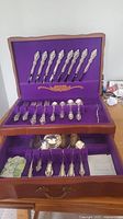 Full view of wooden chest with purple velvet lining and multiple drawers filled with silverplated flatware and serving pieces.