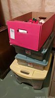 Stack of three plastic bins and one red cardboard box containing Christmas decorations and supplies