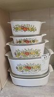 Stack of four white CorningWare casserole dishes with L'echalote La Marjolaine vegetable print design