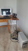 Desk setup with Dell monitor, keyboard, two desktop speakers on wooden table, and Dell tower on floor with connected wires and peripherals.