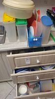 First photo shows the top of three kitchen drawers open with various plastic food storage containers and lids stacked inside and on the countertop above. Containers mostly rectangular and square, with white, yellow, green, blue, and red lids visible.