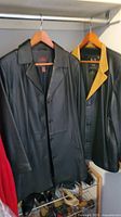 Two leather coats hanging on wooden hangers, one Danier black leather coat and one GV Creazioni black coat with yellow collar lining, both medium size