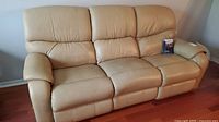 Front view of three-seat tan leather reclining sofa showing overall shape and condition.