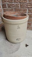 Large beige ceramic crock with '6 Imperial' marking on the front and a reddish-brown clay pot stuck in the opening.