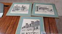 Three framed prints of sketches showing Kingston scenes on floor, with blue mats and gold trim frames.