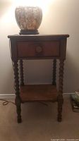 Front view of wooden side table with small drawer and turned legs, showing overall structure and drawer front.