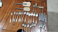 Full layout photo of silverplate cutlery including knives, forks, spoons, and two brushes, arranged on wooden table.