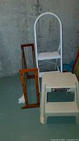 Photo of metal folding step stool, plastic step stool, and wooden extendable rack together against a concrete wall
