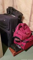 Photo of several stacked suitcases and bags in basement area, showing different sizes and colors including black and red.