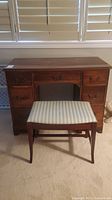 Front view of wooden vanity desk with stool showing drawers and brass handles