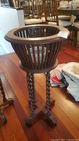 Photo showing full view of vintage wooden plant stand with twisted legs and slatted basket design on three-legged base.