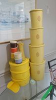 Stack of vintage yellow Tupperware containers, round bowls, small containers, and three plastic shakers.