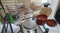 Overview of entire lot including digital scale, various measuring cups, red bowls, white ramekins, and mechanical scale on glass table.