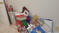 Photo showing a collection of gift bags and boxes stacked against the wall, featuring holiday designs such as teddy bears and snowmen.