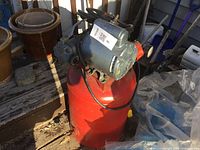 Front side view of red vertical air compressor showing motor and attached hose.