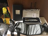 Black padded baby carrier with straps on a white table, with an Amika box and black box insert behind it.