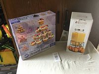 Photo of boxed Olde English 3.5L juice jug with metal stand and Wilton Cupcakes 'N More Dessert Stand packaging on table.