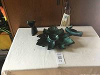 Three Blue Mountain Pottery pieces shown on a white tablecloth: a leaf-shaped dish in the center, a small cat figurine on the left, and a canoe-shaped dish on the right.