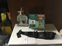 Photo of three items including decorative wall hanger, KIDNASIUM foam bouncy ball in packaging, and black utility belt