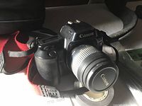 Front angled view of Canon EOS Rebel camera with attached 35-80mm lens showing Canon branding and red strap.