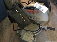 Side view of the Delta chop saw showing attached dust bag, blade guard, and base label.