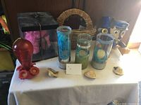 Photo showing three tall glass vases filled with decorative materials, hummingbird feeder, ceramic bird figurines, wicker basket, and dog figurine