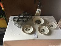 Photo of four decorative plates showing vintage scenes with gold border and six silver-toned glasses in a metal carrier.