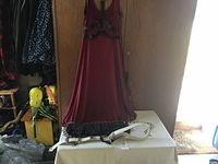 Front view of the burgundy Comic Con dress hanging on a door with the two utility belts placed on a table below it.