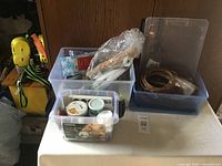 Three bins filled with assorted craft supplies including paint jars, wooden tools, and wreath rings.