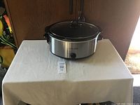 Full view of Crock-Pot slow cooker with lid on white tablecloth, front view showing brand and control knob