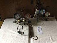 Photo of two Yellow Jacket pressure gauges mounted on a manifold with control knobs and a metal carbide scale on a white cloth surface.