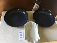 Two large dark blue glazed bowls and one white candy dish placed on a surface
