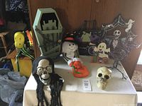 Photo showing the Halloween lot items on a table including coffin decor, ghost and witch figures, skull, skeleton figure, and spider web decoration.