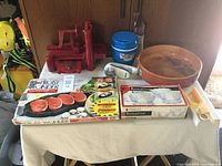 Overview of Frost Wonder meat tenderizer with red parts including handle and base, boxed item featuring images of steak, a wooden bowl, a blue plastic ice bucket cooler, a box of 4 frosted Rosaline glasses, a white rotary grater, and a yellow and white peeler.