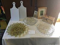 Overview of all items: two white cutting boards, three glass plates, boxed cheese grater, and a framed picture in background