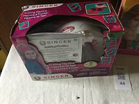 Singer knitting machine in original pink box with visible instruction manual through plastic window.