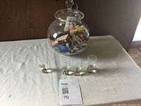 Large glass jug with matches inside and four small glass tumblers arranged in front on a table.