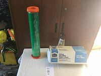Photo showing the green plastic rolled on an orange spool next to its original box labeled 0.31mil Painter's Plastic 9.5ft x 400ft.