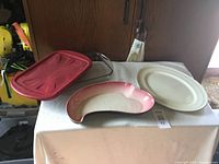 Photo showing the three items on a table: red rectangular casserole dish with glass lid, kidney-shaped pink and cream dish, and white oval platter.
