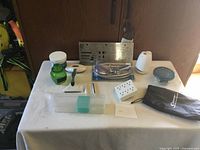 Photo showing various small household and kitchen items on a white surface, including glass jars, power strips, metal stencil, and others.
