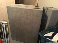 Side view of the twin size folding bed in gray upholstery, folded upright against wall.