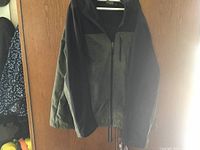 Two-tone jacket in dark grey and black hung on a door, zipper front and zippered chest pocket visible