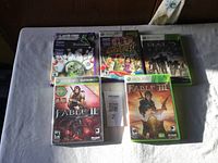 Photo showing five Xbox 360 game cases arranged on a surface, featuring Brunswick Pro Bowling, Kinect Adventures!, Halo: Reach, Fable II, and Fable III.