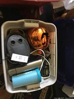 Bin with assorted items showing light-up pumpkin, pump air inflator, insulated tumblers, and charger.